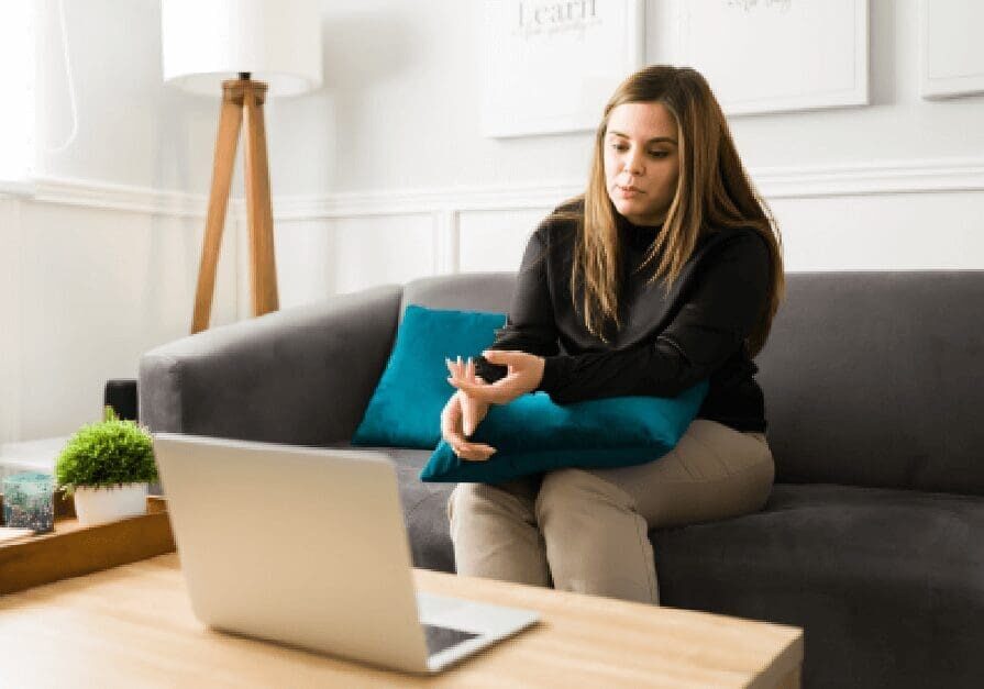 A woman sitting on top of a couch in front of a laptop.